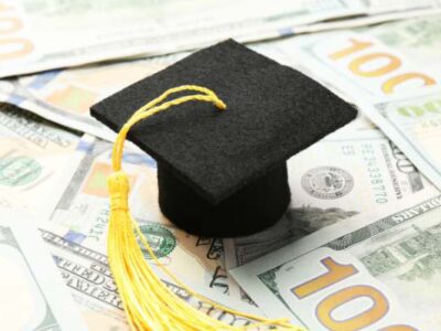 PSU Graduation Cap on a pile of 100 dollar bills