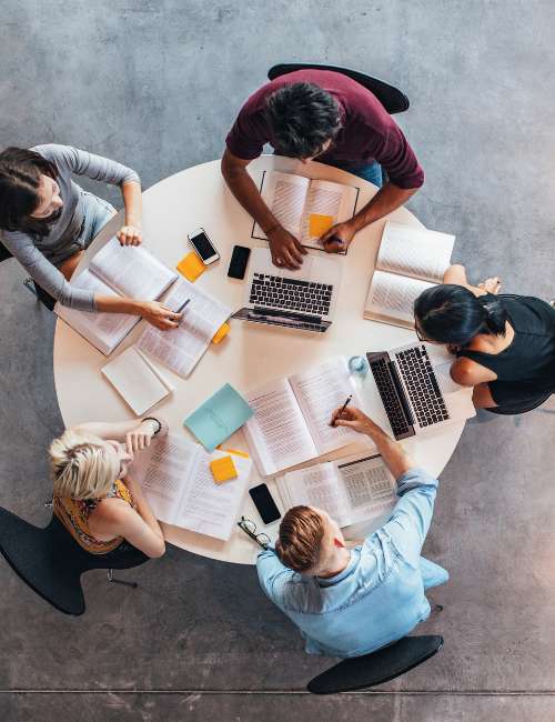 Group of public health graduate students studying together at a circular table with their laptops and textbooks out on the desk.